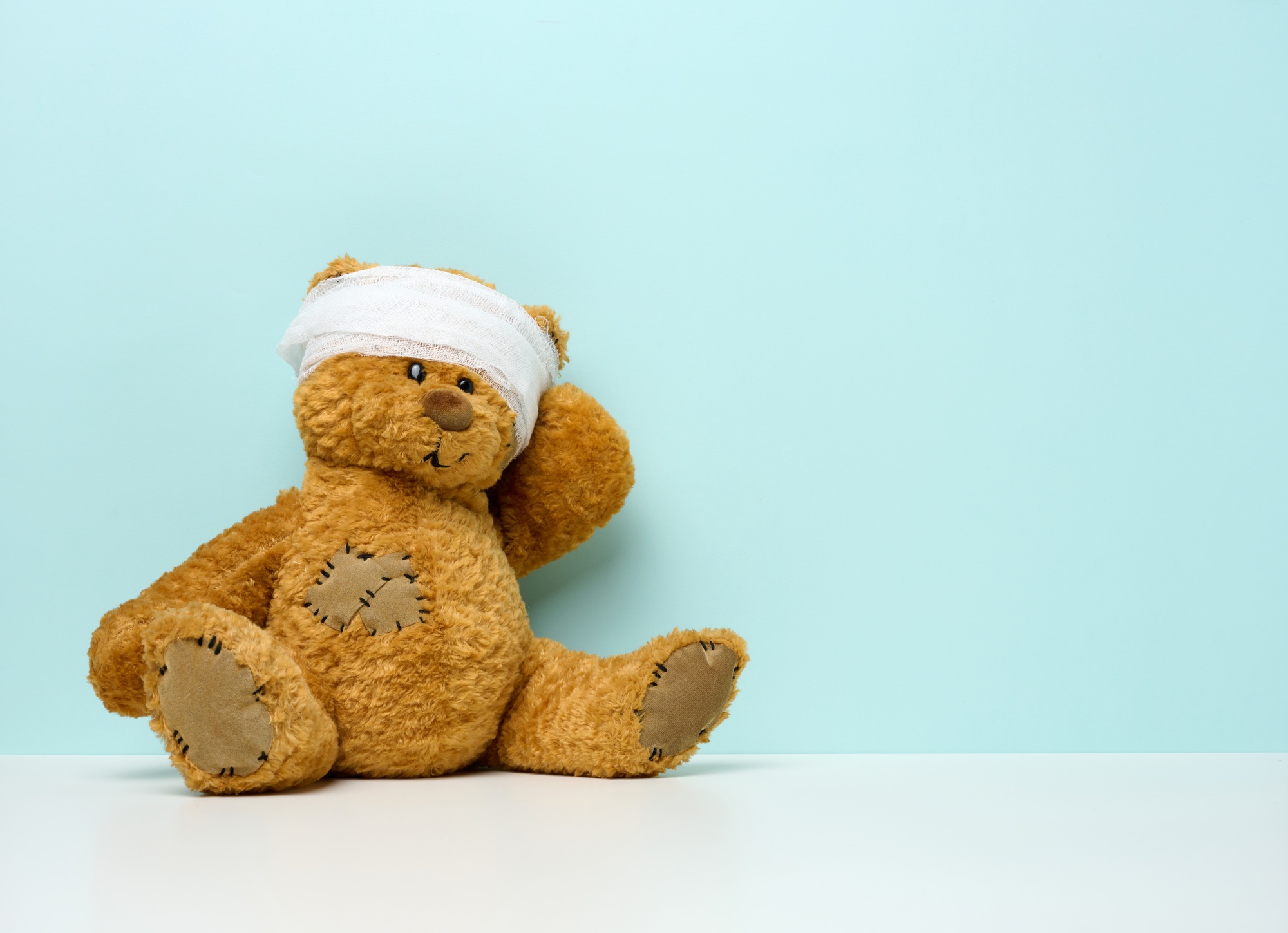 Children's toy teddy bear sits with a bandaged head. Childhood trauma concept